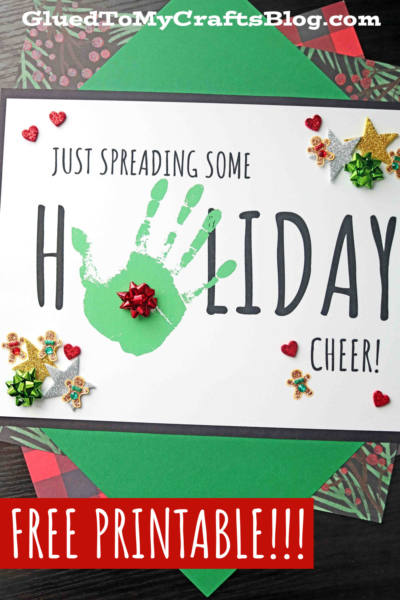 A festive holiday card reads Just spreading some handprint holiday cheer! with holiday featuring a green handprint as the O. The card is decorated with small bows, hearts, stars, and gingerbread stickers. Free printable!!! is written below.