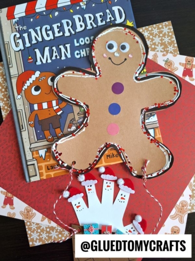 Children’s book “The Gingerbread Man Loose at Christmas” with a gingerbread man hot air balloon craft, festive papers, and a handprint Santa craft, all arranged on a dark surface. @GLUEDTOMYCRAFTS is labeled at the bottom.