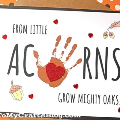 A handmade mighty oaks keepsake card reads “From little acorns grow mighty oaks!” with “ACORNS” in large letters, a brown handprint as the O, red hearts, and small drawings of acorns and an oak leaf.
