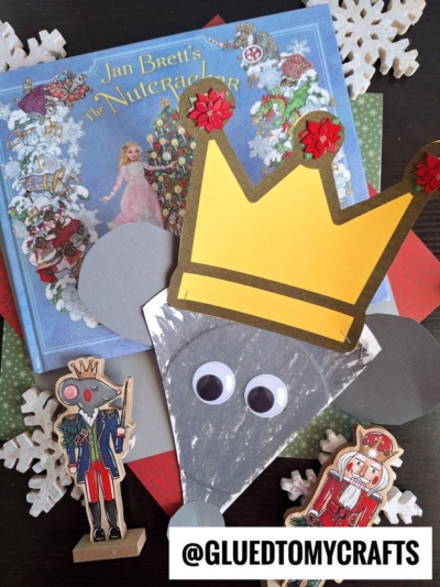 A paper plate mouse king with a paper crown, big googly eyes, and gray ears sits among Nutcracker-themed decor and Jan Brett’s The Nutcracker book. @GLUEDTOMYCRAFTS label is at the bottom.