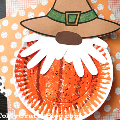 A paper plate craft featuring a scarecrow pumpkin gnome with a brown hat and white beard, decorated with orange and black polka dot papers in the background.