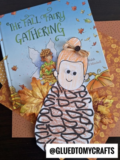 A children’s book titled The Fall Fairy Gathering is displayed with a fall-themed paper craft of a pine cone fairy decorated with autumn leaves and an orange background. @GLUEDTOMYCRAFTS is written at the bottom.