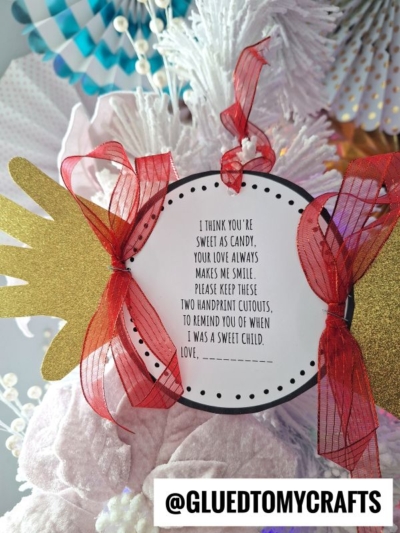 A round tag with a sentimental Handprint Candy Poem is decorated with gold handprint cutouts and a red ribbon, attached to a white textured background. The tag reads: “I think you’re sweet as candy…” The @GLUEDTOMYCRAFTS tag is at the bottom.