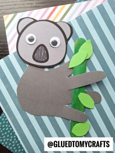 A handmade sloth craft using gray paper for the body and handprint koala style, googly eyes, green leaves, and a green stick, placed on colorful striped paper backgrounds. @GLUEDTOMYCRAFTS is at the bottom.