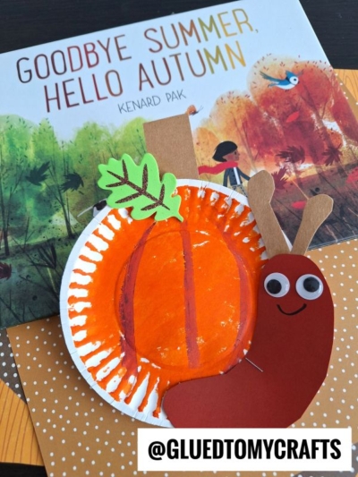 A children’s book titled Goodbye Summer, Hello Autumn sits behind a charming paper plate pumpkin snail craft, featuring a smiling snail made from paper, a googly eye, and a paper plate. @GLUEDTOMYCRAFTS is written below.