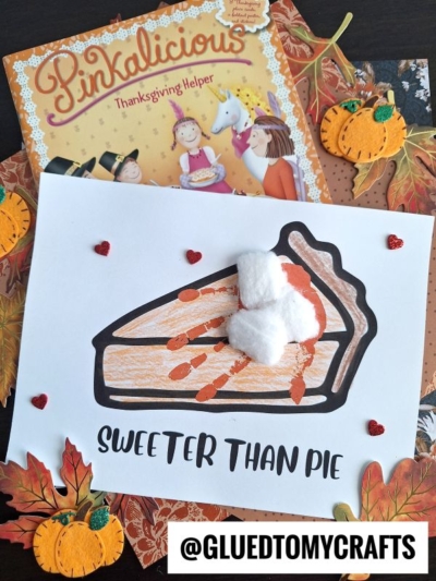 A children’s book titled “Pinkalicious: Thanksgiving Helper” lies behind a craft with a pie drawing, cotton ball “whipped cream,” heart stickers, fall leaves, pumpkin decorations, and a cute handprint pie. Text reads “Sweeter Than Pie.”.