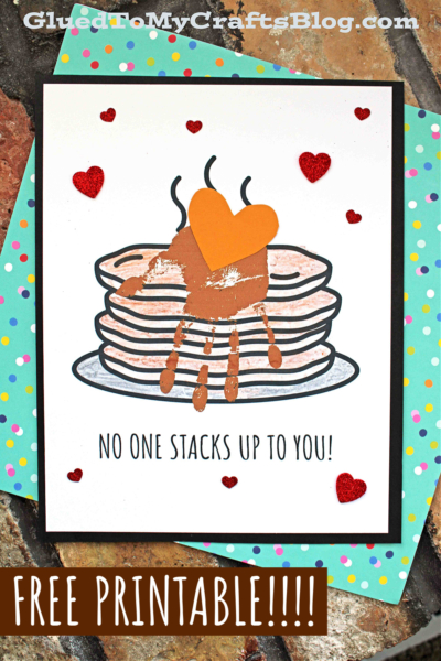 A handmade card with a stack of handprint pancakes featuring a brown handprint and orange paper heart on top, surrounded by red glitter hearts. Text below reads, “NO ONE STACKS UP TO YOU!” with “FREE PRINTABLE!!!!” at the bottom.