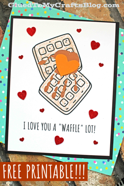 A sweet card featuring two waffles topped with chocolate and an orange heart, surrounded by red glitter hearts. Inspired by a handprint waffle keepsake, it reads I LOVE YOU A WAFFLE LOT! with FREE PRINTABLE!!! at the bottom.
