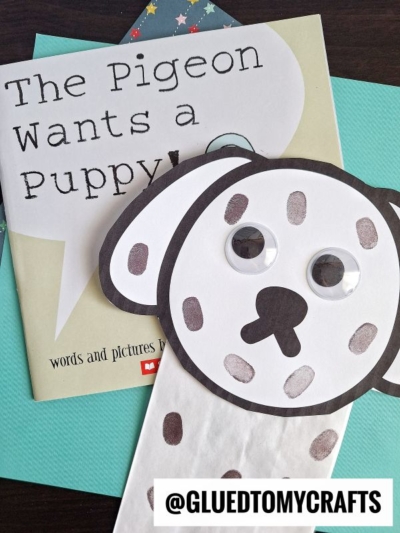 A children’s book titled The Pigeon Wants a Puppy! sits beside a paper bag dalmatian craft with googly eyes and spots. The Instagram handle @GLUEDTOMYCRAFTS is at the bottom.