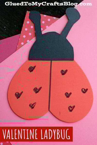 A handmade Valentine ladybug craft made from red and black paper, with heart shapes drawn on its wings, placed on pink and red paper backgrounds—perfect for heart shaped crafts or valentine art project ideas. Text reads VALENTINE LADYBUG at the bottom.