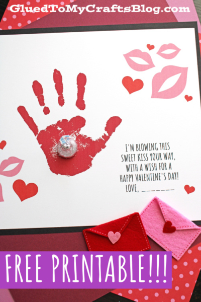 A Valentine’s Day card features a red handprint, a chocolate kiss, pink lips, and hearts—a sweet kiss keepsake. Text reads: “I’m blowing this sweet kiss your way, with a wish for a happy Valentine’s Day! Love, ____.” “FREE PRINTABLE!!!” at the bottom.