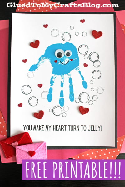 A handmade Valentine’s card features a blue handprint jellyfish with googly eyes, surrounded by bubbles and red glitter hearts. Below, the text reads “You make my heart turn to jelly!” on a crisp white background.
