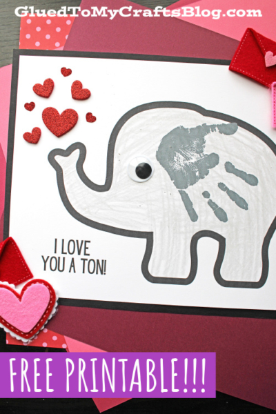A handmade card featuring a gray handprint valentine elephant with a child’s handprint as its ear, red heart decorations, and the text “I LOVE YOU A TON!” on white paper, with “FREE PRINTABLE!!!” at the bottom.