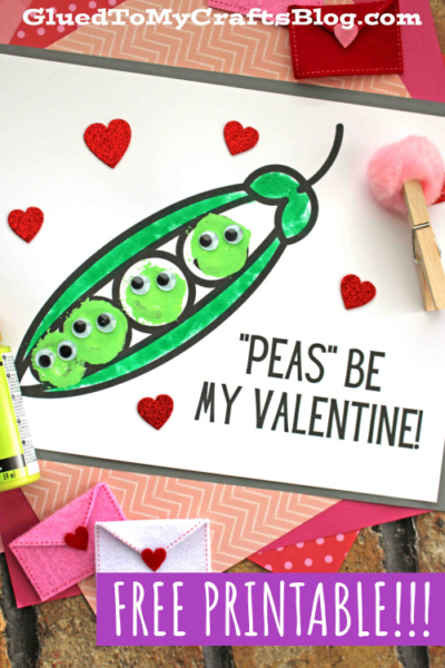 A Valentine’s card featuring pea pods with googly eyes, red heart decorations, and the message “peas be my valentine!” sits surrounded by craft supplies and colorful envelopes.