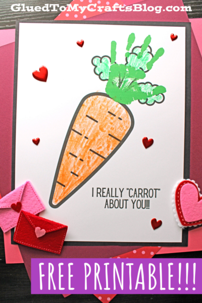 A handmade Valentine’s card featuring a handprint carrot keepsake with leafy green tops made from a child’s green handprints. The text says “I REALLY ‘CARROT’ ABOUT YOU!” and the card is decorated with felt hearts and envelopes.