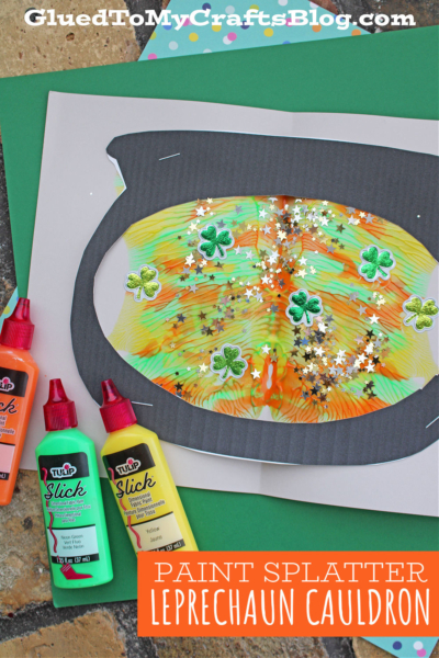 A colorful Paint Splat Leprechaun Cauldron craft is shaped like a leprechaun’s pot, adorned with shamrock and star confetti. Three puffy paint bottles in orange, yellow, and green are nearby. Text reads: “Paint Splatter Leprechaun Cauldron.”.