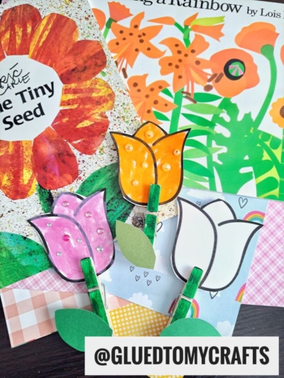 Handmade Clothespin Tulip Flower crafts with green stems and leaves are displayed on patterned paper backgrounds, alongside colorful floral children’s books and a tag reading “@GLUEDTOMYCRAFTS” in bold text.