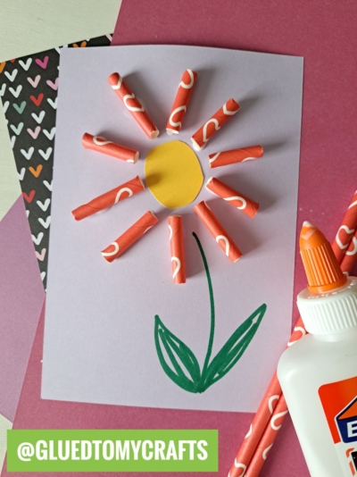 A handmade flower kids craft with a yellow circle center and petals from red-and-white paper straw pieces, glued onto purple paper with a green drawn stem and leaves—perfect for anyone seeking creative flower craft ideas.
