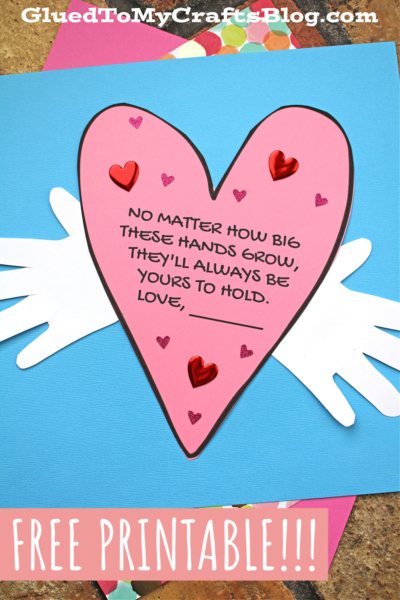 A pink handprint heart with a handwritten message, always be yours, is decorated with red heart stickers and placed over two white paper hands on a blue background. The text at the top reads, GluedToMyCraftsBlog.com. Banner: Free Printable!!!.