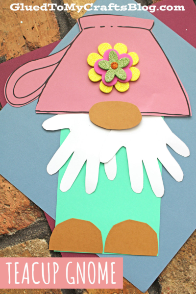 A colorful paper craft teacup gnome features a pink teacup hat, white beard, brown nose and shoes, mint green body, and a decorative yellow and purple flower on the hat. Text reads “TEACUP GNOME.”.