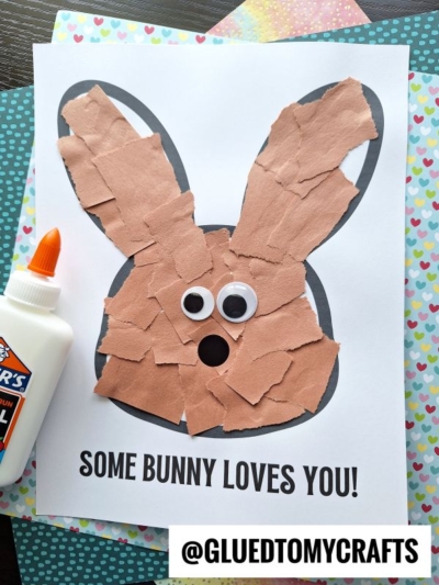 A torn paper bunny craft featuring brown paper pieces glued onto a bunny outline, complete with googly eyes and a black nose and mouth. Text reads “SOME BUNNY LOVES YOU!” with the username @GLUEDTOMYCRAFTS below.
