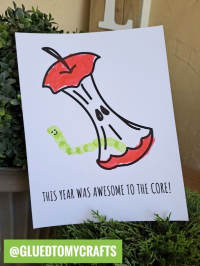A drawing of an apple core with a green fingerprint worm craft as the caterpillar. Text below reads, THIS YEAR WAS AWESOME TO THE CORE! Green label at the bottom says @GLUEDTOMYCRAFTS.