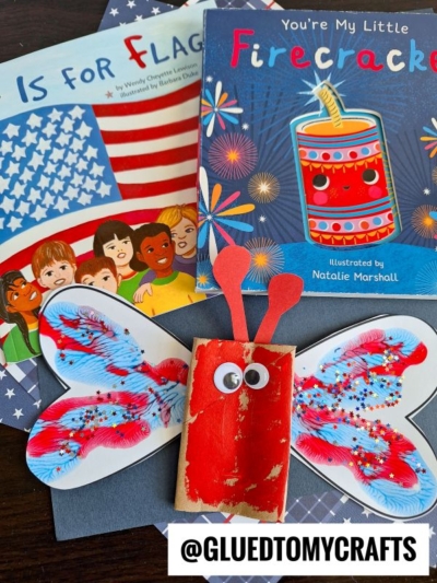 Children’s books “A is for Flag” and “You’re My Little Firecracker” are shown with a patriotic toilet paper roll butterfly craft, featuring painted paper wings, a red-painted cardboard body, googly eyes, and red pipe cleaner antennae.