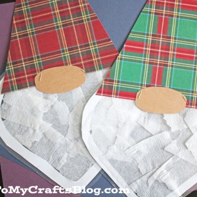 Two paper gnome suncatchers with plaid hats and white tissue paper beards rest on colorful construction paper.