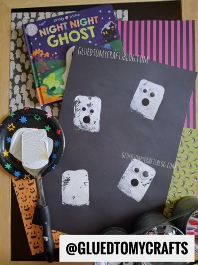 Children’s ghost craft with a Night Night Ghost book, paint, spatula, paint plate, and Halloween paper. White spatula stamped crafts feature prints with googly eyes arranged on black paper to look like ghosts. @gluedtomycrafts.