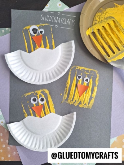 Two yellow chick spatula stamped crafts feature painted spatula prints, paper plate wings, googly eyes, and orange paper beaks on a gray sheet. Nearby are craft materials and a painted spatula.