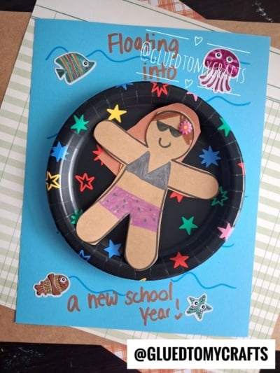 A paper plate craft of a smiling person in sunglasses and a swimsuit relaxing on a playful pool floatie art, floating in water and surrounded by colorful fish, stars, and sea creatures, with the text Floating into a new school year!.