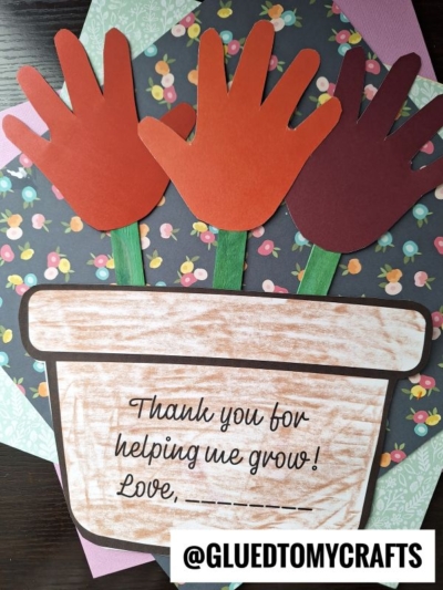 A craft showing three handprint cutouts as flowers in a paper flower pot with the message, Thank you for helping me grow! Love, ___. Colorful paper serves as a background. @GLUEDTOMYCRAFTS tag is at the bottom.