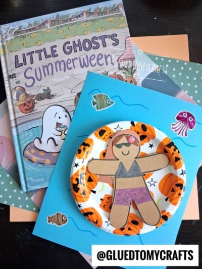 A children’s book titled “Little Ghost’s Summerween” sits beside a Halloween-themed craft of a paper ghost with a pool floatie art swimsuit on a pumpkin-patterned plate, surrounded by sea-themed stickers and paper. @GLUEDTOMYCRAFTS is labeled at the bottom.