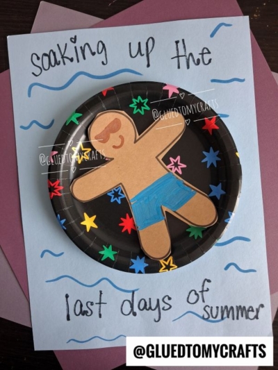 A paper gingerbread figure with sunglasses and blue shorts on a star-decorated paper plate, accompanied by playful pool floatie art, with the words soaking up the last days of summer written on blue paper.
