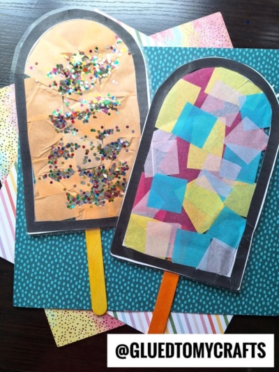 Two colorful paper popsicle crafts, one a sparkling popsicle suncatcher with gold tissue and glitter, the other with multicolored tissue squares, both on patterned sheets. @GLUEDTOMYCRAFTS is written at the bottom.