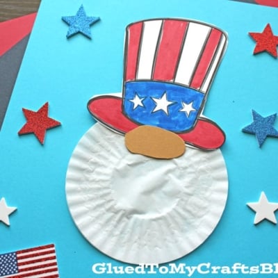 A cupcake liner gnome craft with a white beard, a hat in U.S. flag colors, and foam star decorations on blue paper.