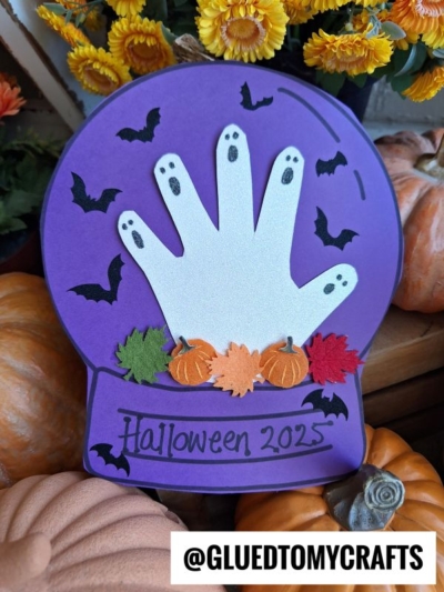 This Halloween craft features a handprint ghost, bats, pumpkins, and leaves inside a festive halloween snow globe with “Halloween 2025” written on it. Pumpkins and flowers decorate the background, while @GLUEDTOMYCRAFTS is displayed at the bottom.