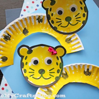 Two adorable paper plate leopards with googly eyes, black spots, and hand-drawn faces sit on colorful polka dot backgrounds. One leopard sports a cute pink bow near its ear.