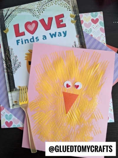 A pink paper features a chick made with yellow fork painting crafts, heart stickers for eyes, and an orange beak. Behind it sits a book titled LOVE Finds a Way. @GLUEDTOMYCRAFTS is written at the bottom.