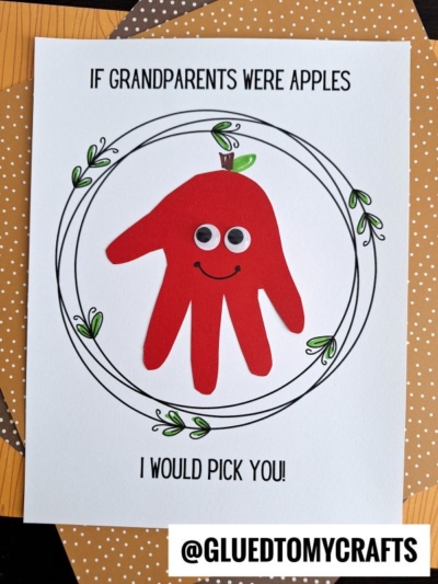 A card featuring a charming handprint apple with a red handprint shaped like an apple, googly eyes, and a smile—perfect for Grandparent’s Day. The text reads, IF GRANDPARENTS WERE APPLES I WOULD PICK YOU! Decorative leaves and the handle @GLUEDTOMYCRAFTS are also visible, making this handprint apple craft a heartfelt keepsake.