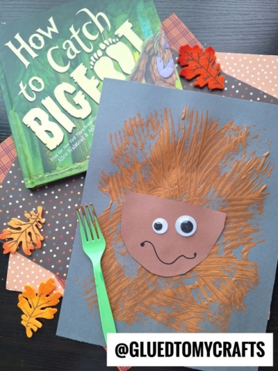 A children’s craft project shows a brown painted creature with googly eyes, beside a green fork, autumn leaves, patterned paper, and the book How to Catch Bigfoot—perfect for inspiring creative fork painting crafts.