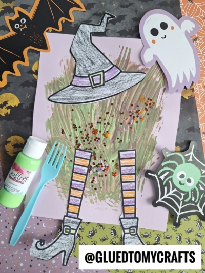 A Halloween craft scene featuring a fork painted melted witch’s hat and legs, a spooky ghost, bat, spider, green paint, plastic fork, and colorful patterned paper, with the text @GLUEDTOMYCRAFTS at the bottom.