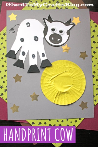 A fun children's craft featuring a handprint cow made from white paper with black spots and googly eyes, surrounded by gold stars and a yellow circle on a gray background. Text at the top reads GluedToMyCraftsBlog.com.