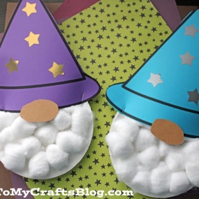 A charming paper plate wizard craft featuring a purple hat with yellow stars, a round paper nose, and a fluffy cotton ball beard, all displayed on colorful patterned paper.
