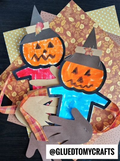 Two paper scarecrow crafts with jack-o-lantern faces, blue and red shirts, brown hats, and decorative fall paper backgrounds. Plaid ribbon and cutout paper hands create a sweet scarecrow hug. Text reads @GLUEDTOMYCRAFTS.