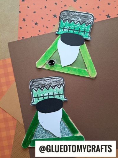 Two Frankenstein monster crafts, including a playful Frankenstein gnome, are made from green painted craft sticks, paper, and markers and sit on brown paper. An artificial googly eye accent is placed on one. GLUEDTOMYCRAFTS is labeled at the bottom.