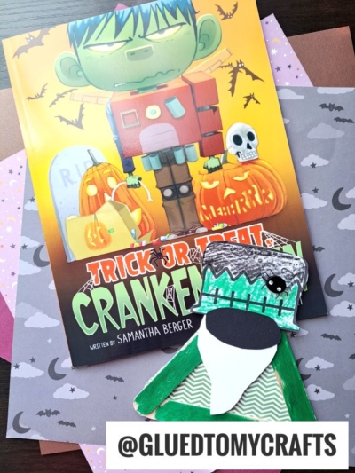 A Halloween children’s book titled Trick or Treat, Crankenstein sits on colored paper with a handmade green Frankenstein gnome craft and the handle @GLUEDTOMYCRAFTS at the bottom.