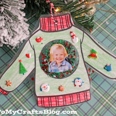A handmade christmas sweater ornament displays a child’s photo in the center, decorated with festive holiday stickers.
