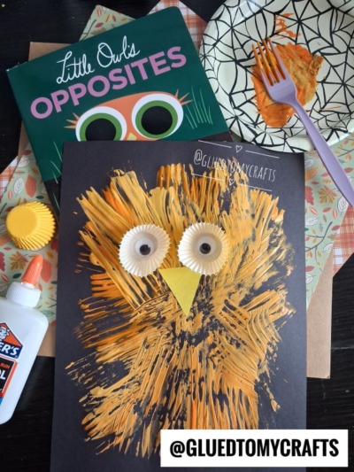 A fork painted owl children’s craft made with orange paint and cupcake liners on black paper. Supplies include glue, a fork, the book “Little Owls Opposites,” and a paper plate with paint. @GLUEDTOMYCRAFTS is written at the bottom.