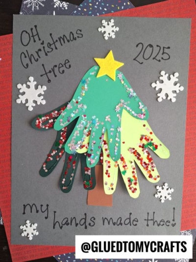 A Christmas tree made from three paper handprints, decorated with glitter and a yellow star, surrounded by snowflake stickers—this charming craft is the perfect christmas keepsake, with "OH Christmas tree 2015 my hands made thee!" written on gray paper.